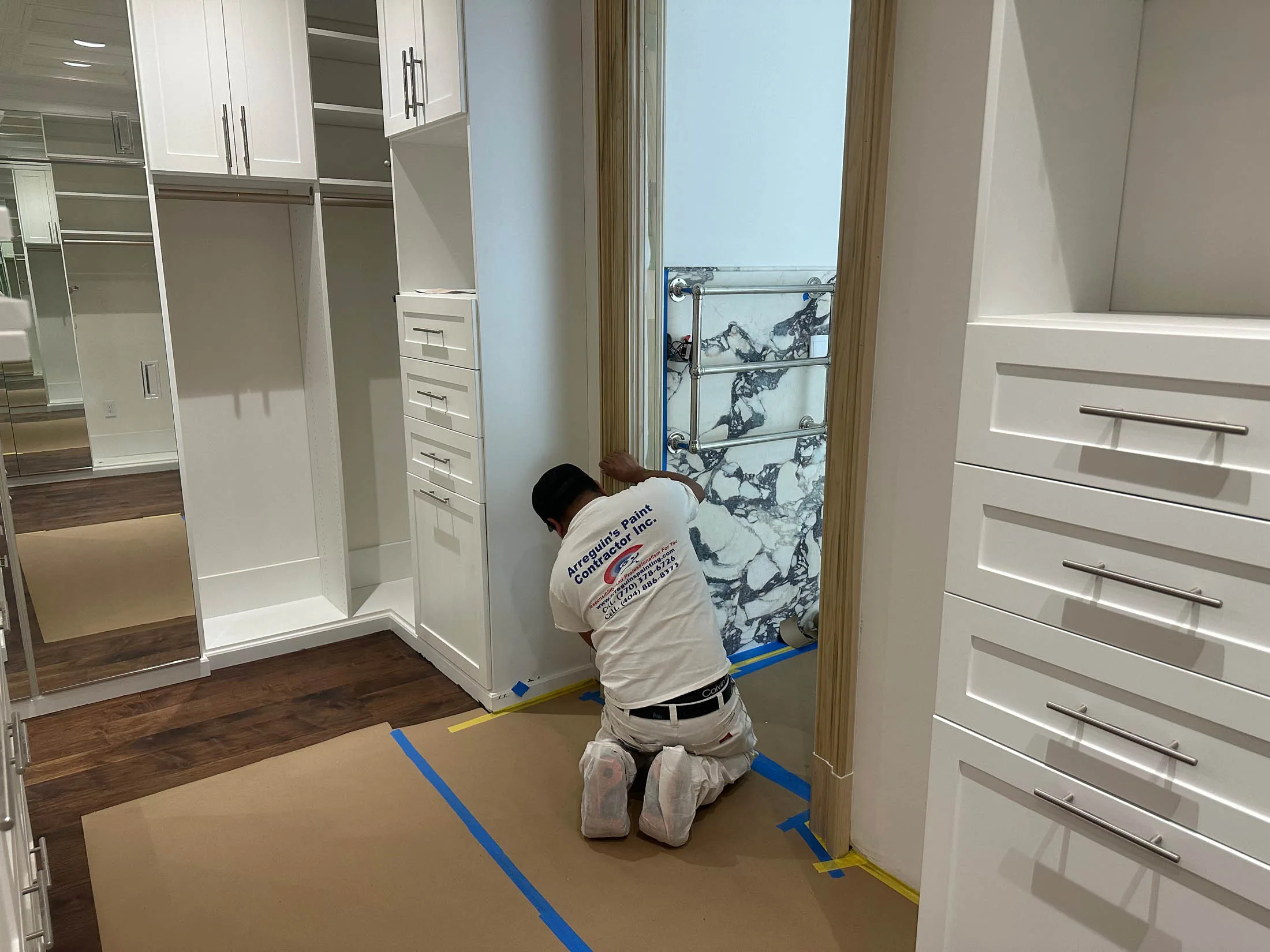 Professional painter applying finishing touches in a modern closet space with white cabinetry and wooden flooring, showcasing Arreguin's Painting services for residential cabinet refinishing in Marietta, GA.