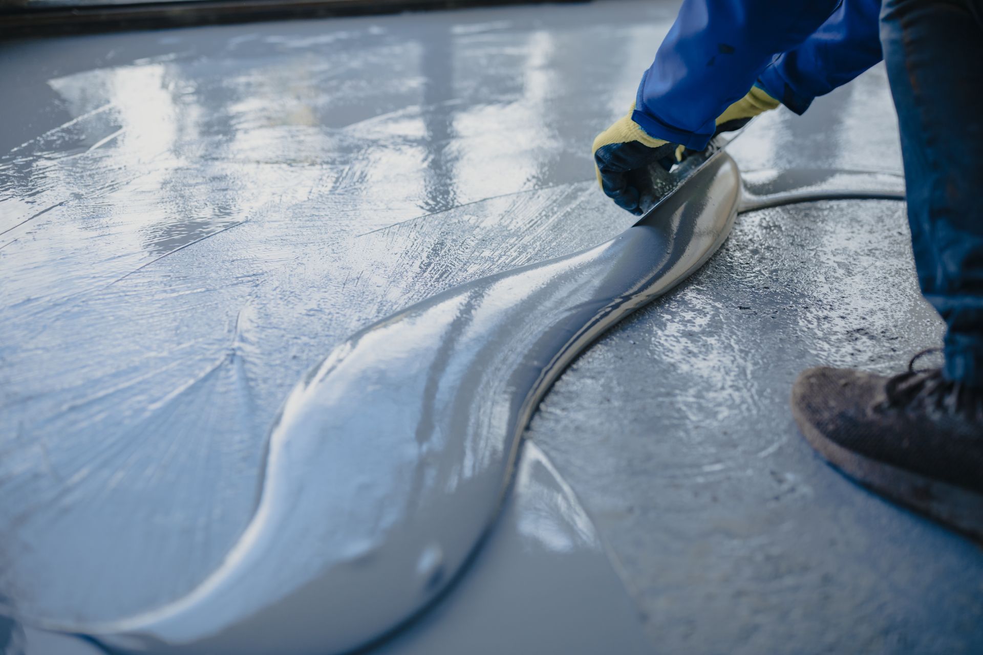 A person in protective gloves spreads liquid cement or epoxy with a trowel over a floor surface.