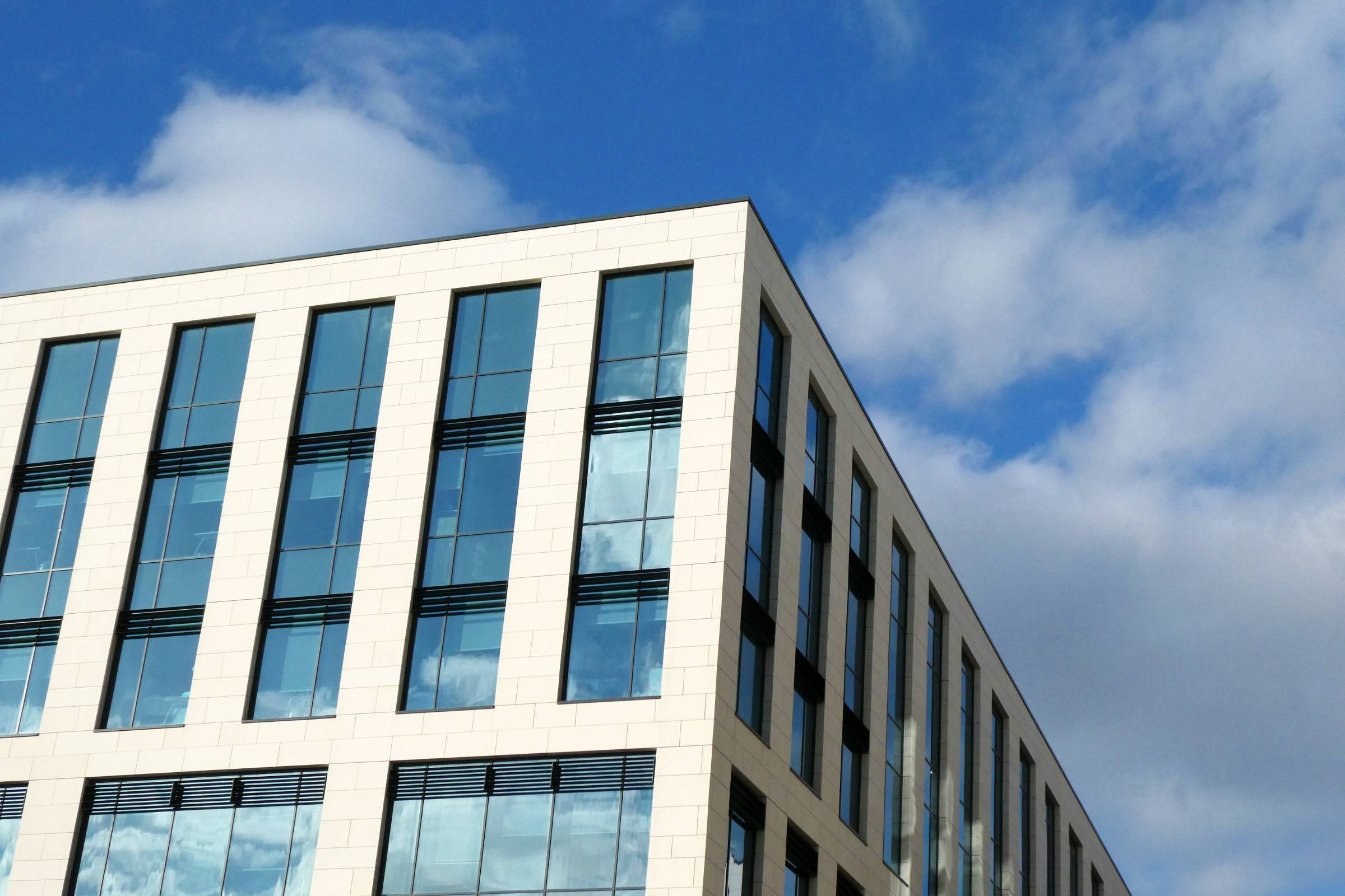Modern office building with large glass windows and white exterior walls, featuring fresh new construction painting, set against a blue sky with scattered clouds.