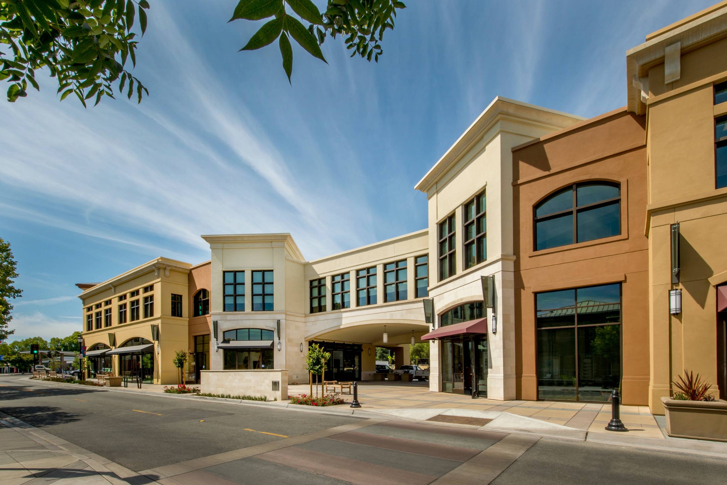 A modern commercial building with large windows and tan, beige, and brown facades—enhanced by expert New Construction Painting—lines a quiet street under a clear blue sky.